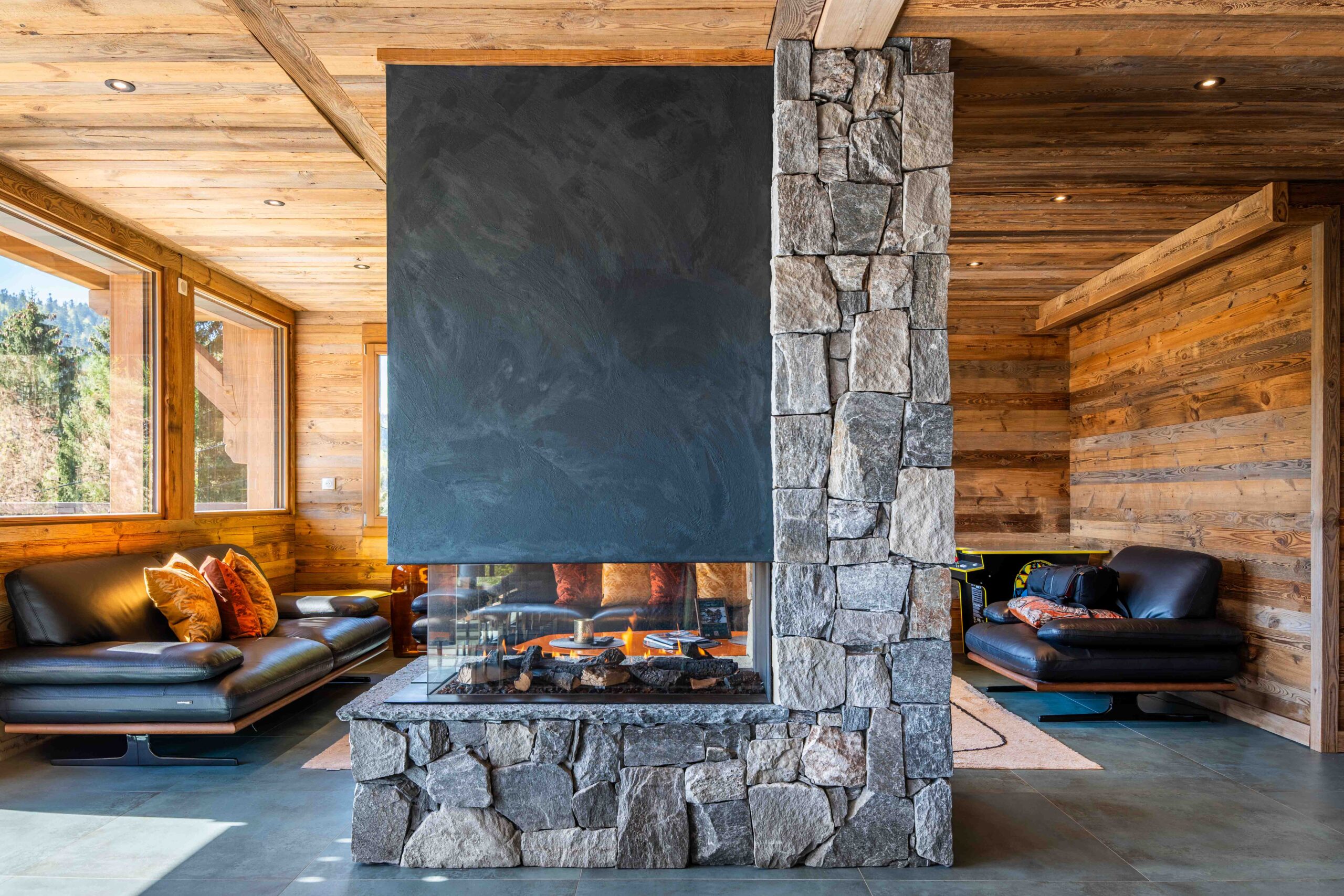 Cheminée centrale en pierre dans un salon en bois avec canapés en cuir, dans un gîte haut de gamme des Vosges