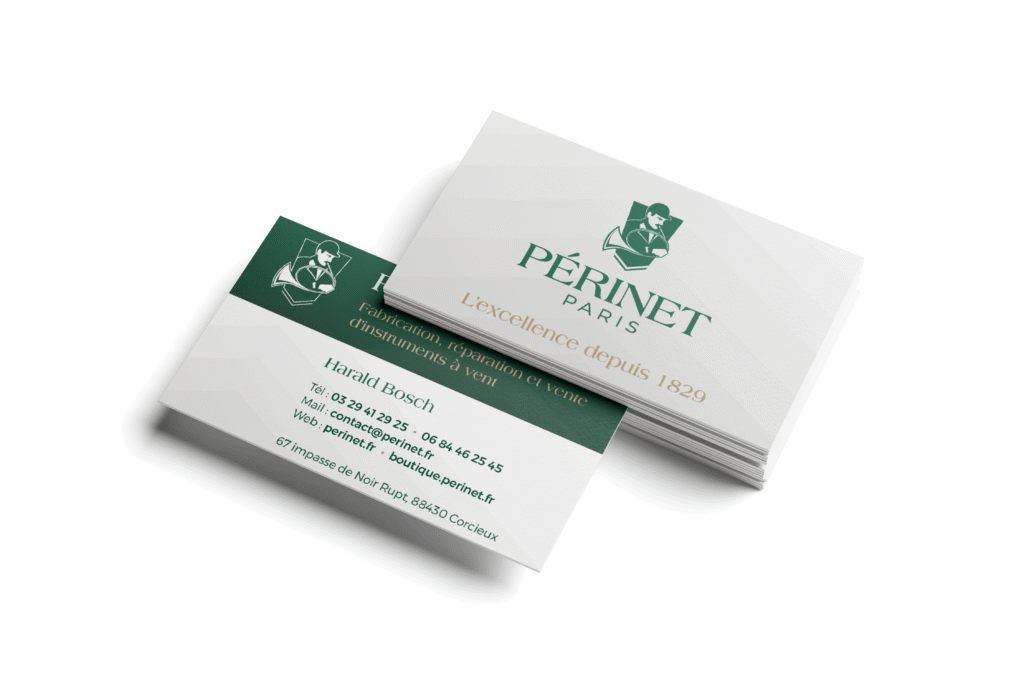 Un mockup de la carte de visite de Périnet Paris. Le recto est posée sur une pile avec le verso, montrant le logo Périnet vert et la mention "L'excellence depuis 1829". L'autre est légèrement inclinée, affichant les coordonnées : nom, téléphone, email, sites web et adresse physique.